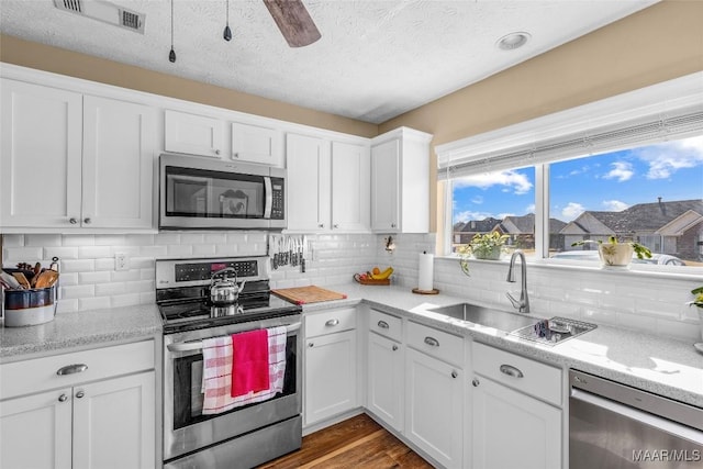 kitchen with stainless steel appliances, white cabinetry, backsplash, and sink