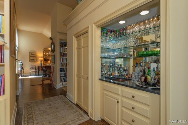 bar featuring vaulted ceiling, dark hardwood / wood-style flooring, dark stone counters, cream cabinetry, and sink