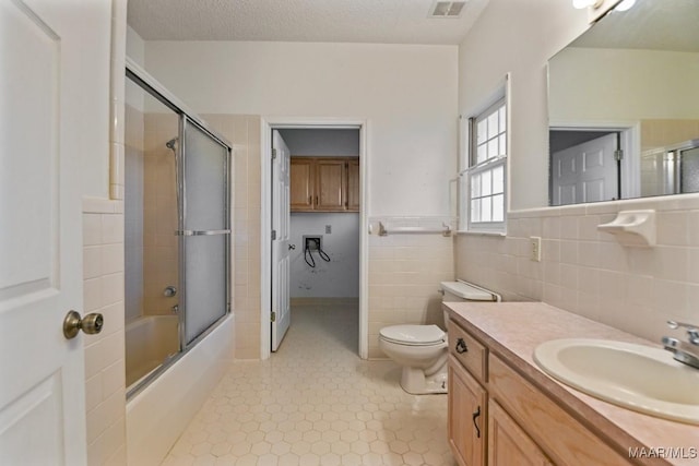 full bathroom featuring toilet, enclosed tub / shower combo, vanity, tile walls, and a textured ceiling