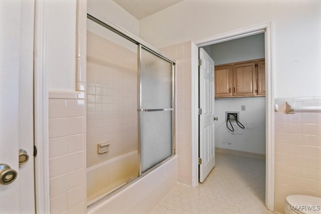 bathroom with tile walls, enclosed tub / shower combo, and toilet