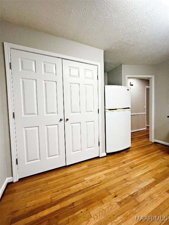 unfurnished bedroom featuring a textured ceiling, light hardwood / wood-style flooring, white fridge, and a closet