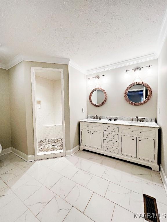 bathroom featuring a textured ceiling, ornamental molding, tiled shower, and vanity