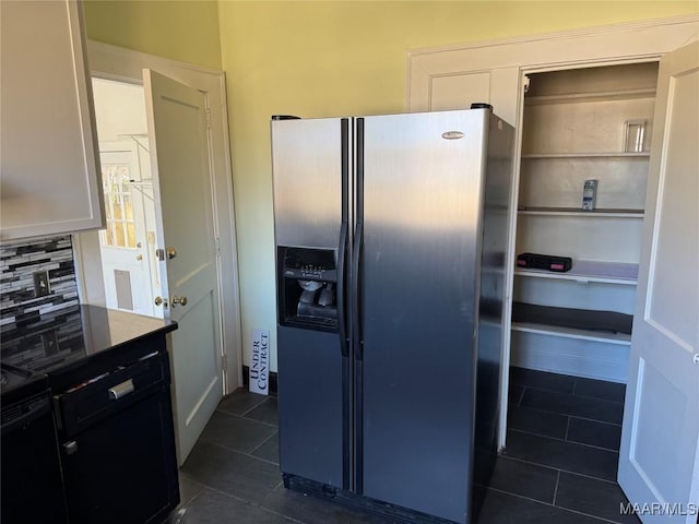 kitchen featuring dark tile patterned flooring, stainless steel refrigerator with ice dispenser, white cabinetry, decorative backsplash, and black electric range