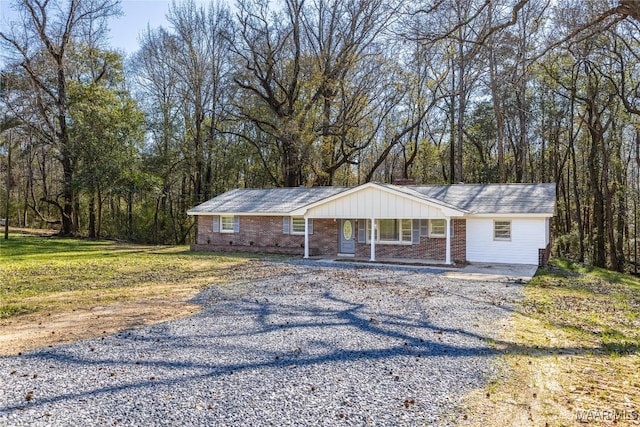 ranch-style home featuring a porch, gravel driveway, brick siding, and a front yard