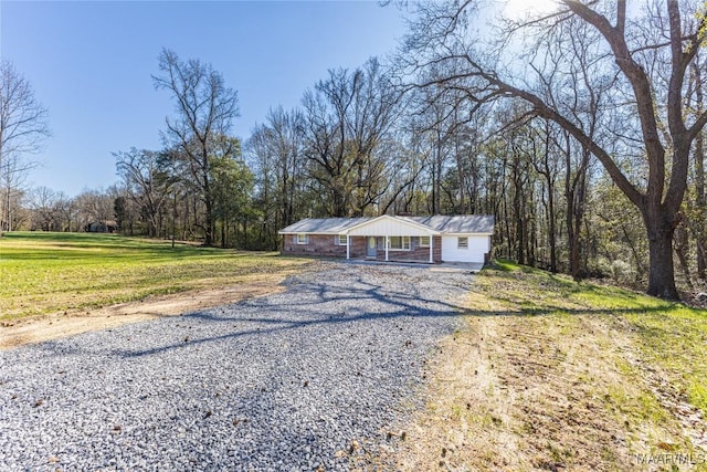 ranch-style home featuring gravel driveway and a front yard