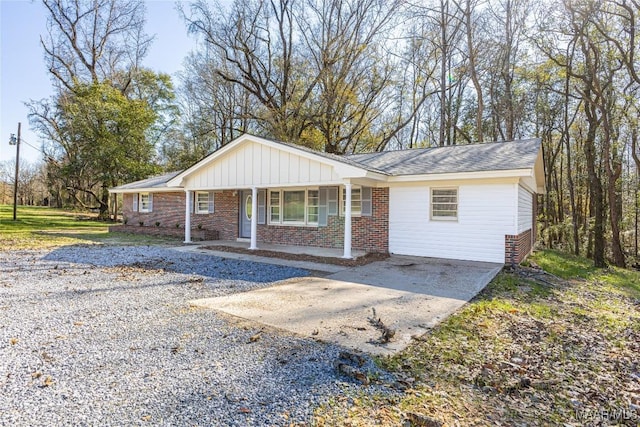 single story home featuring a porch, concrete driveway, brick siding, and board and batten siding