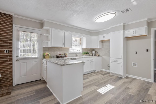 kitchen with a sink, light wood-style floors, white cabinets, light stone countertops, and open shelves