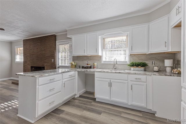 kitchen featuring a wealth of natural light, white cabinets, a sink, light wood-type flooring, and a peninsula