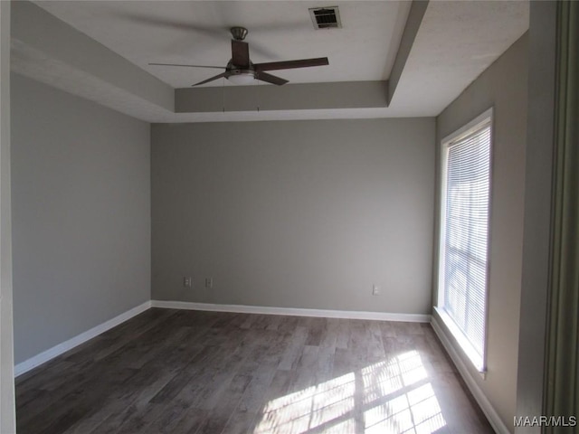 empty room featuring dark wood finished floors, a raised ceiling, visible vents, and a wealth of natural light