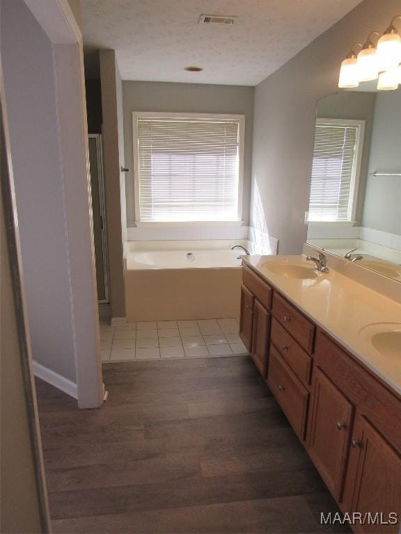 full bath featuring visible vents, double vanity, a sink, a textured ceiling, and a bath