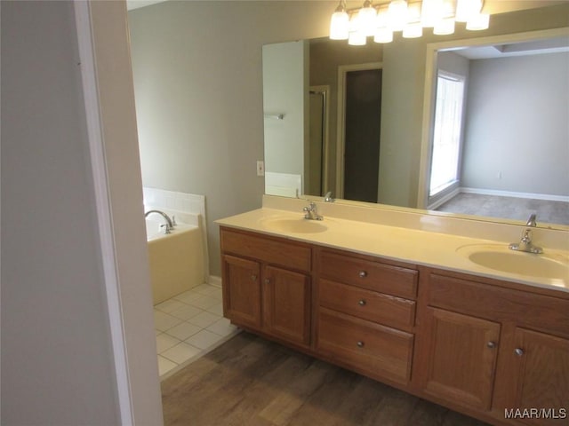 full bathroom featuring double vanity, wood finished floors, a garden tub, and a sink