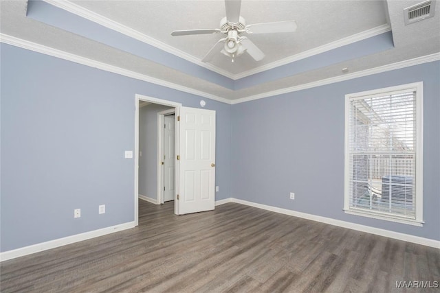 empty room with a textured ceiling, ceiling fan, a tray ceiling, dark hardwood / wood-style flooring, and ornamental molding