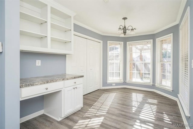 interior space with a notable chandelier, pendant lighting, ornamental molding, dark hardwood / wood-style flooring, and white cabinetry