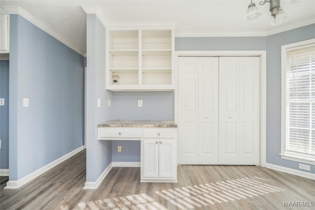 kitchen with built in desk, a healthy amount of sunlight, white cabinetry, and ornamental molding