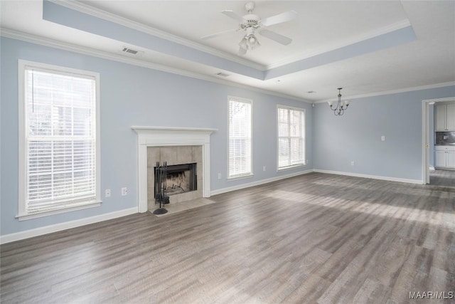 unfurnished living room featuring a raised ceiling, a tiled fireplace, ceiling fan with notable chandelier, wood-type flooring, and crown molding