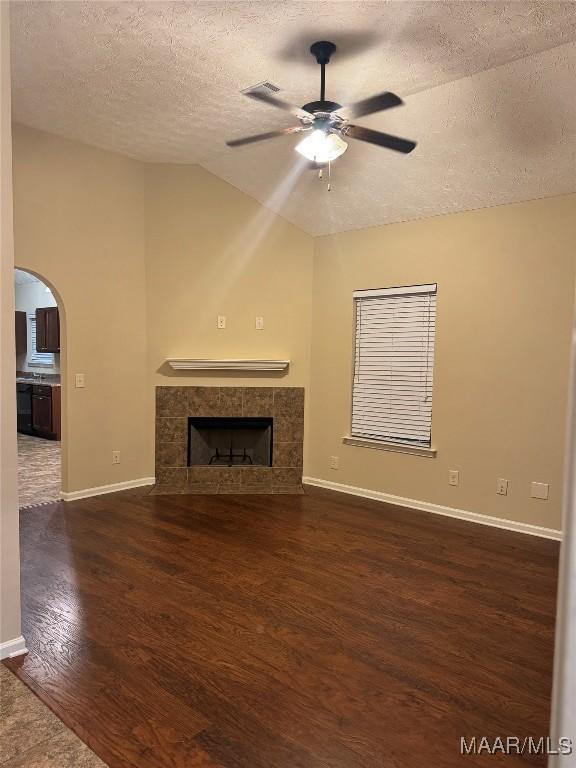 unfurnished living room with a textured ceiling, lofted ceiling, dark wood-type flooring, ceiling fan, and a tiled fireplace