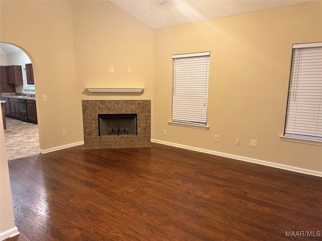 unfurnished living room featuring lofted ceiling, dark hardwood / wood-style floors, and a tile fireplace