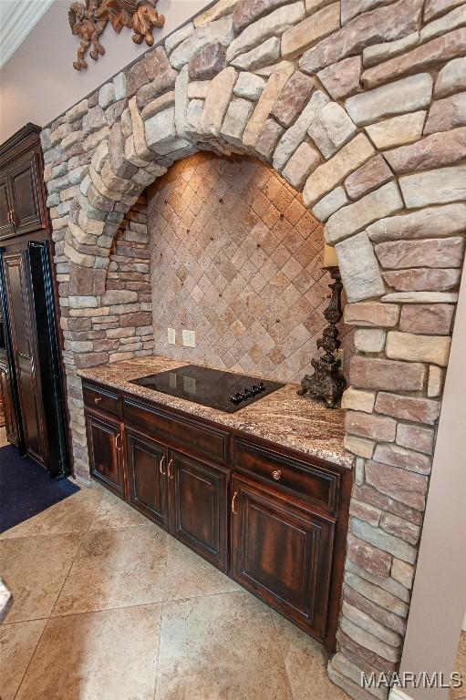 kitchen with dark brown cabinetry, light stone countertops, black electric cooktop, and ornamental molding