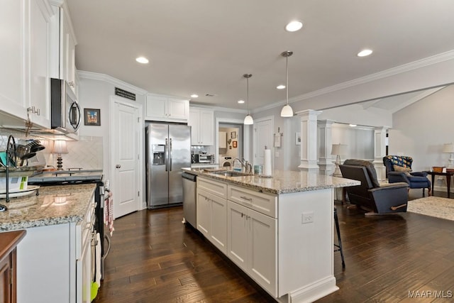 kitchen with white cabinets, appliances with stainless steel finishes, an island with sink, and decorative columns