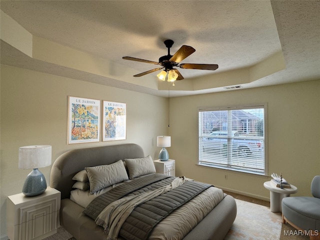 bedroom featuring ceiling fan, a textured ceiling, and a tray ceiling