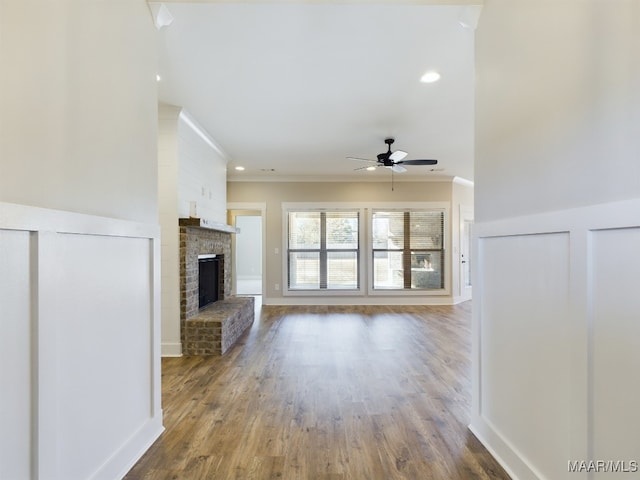 unfurnished living room featuring a brick fireplace, hardwood / wood-style floors, ornamental molding, and ceiling fan