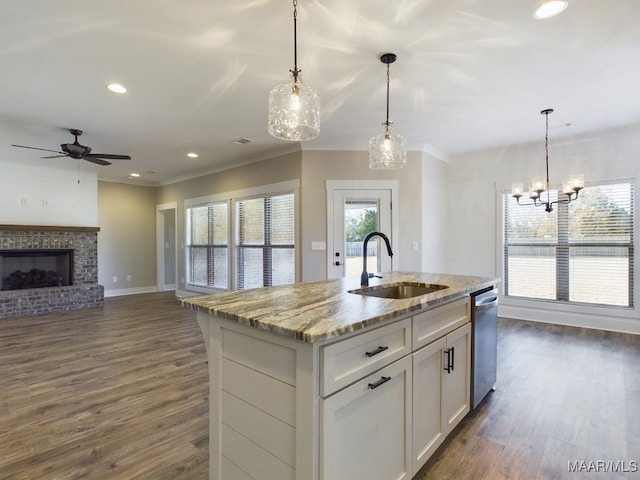 kitchen featuring dishwasher, sink, white cabinets, light stone counters, and a center island with sink