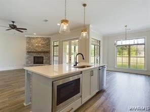 kitchen with a stone fireplace, stainless steel appliances, a sink, open floor plan, and an island with sink