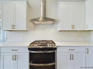 kitchen featuring wall chimney range hood, white cabinetry, light countertops, and stainless steel range with gas stovetop