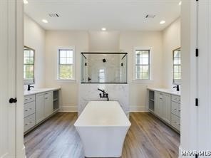 bathroom with a stall shower, two vanities, baseboards, and wood finished floors