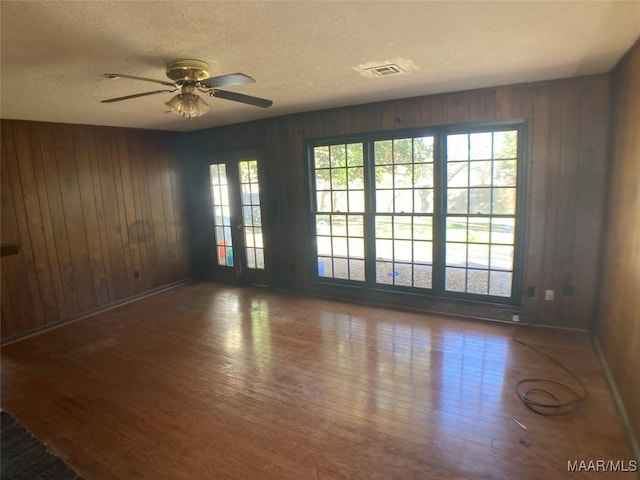 empty room featuring a textured ceiling, ceiling fan, wood-type flooring, and wooden walls