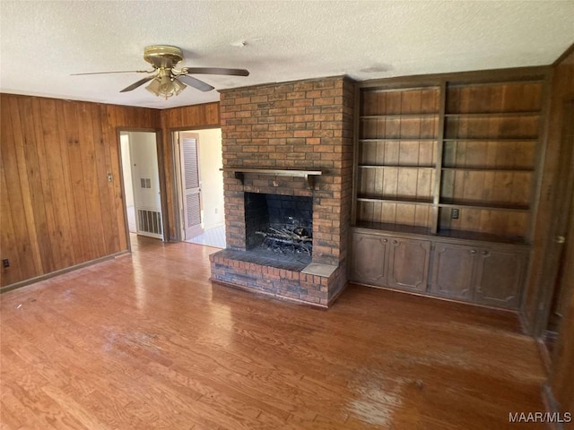 unfurnished living room with ceiling fan, a textured ceiling, wood walls, and a fireplace