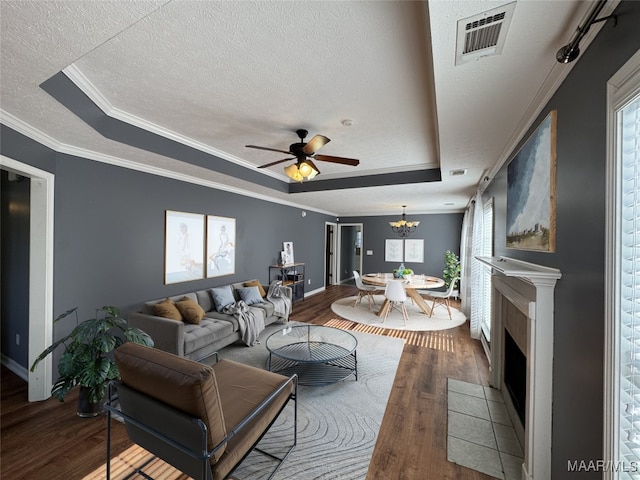 living room featuring ceiling fan with notable chandelier, hardwood / wood-style floors, ornamental molding, a raised ceiling, and a tiled fireplace