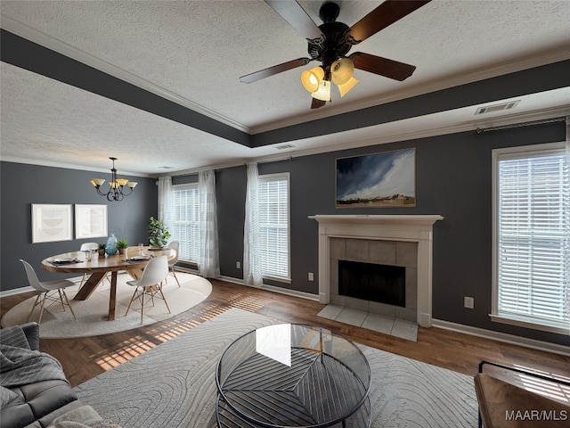 living room featuring hardwood / wood-style flooring, ornamental molding, a tiled fireplace, and a tray ceiling