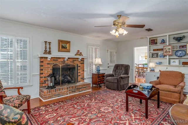 living room with ceiling fan, crown molding, a fireplace, and hardwood / wood-style floors