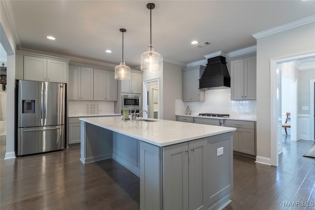 kitchen with custom exhaust hood, stainless steel appliances, hanging light fixtures, gray cabinetry, and a center island with sink