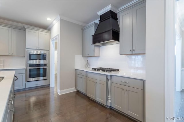 kitchen featuring appliances with stainless steel finishes, decorative backsplash, premium range hood, ornamental molding, and gray cabinetry