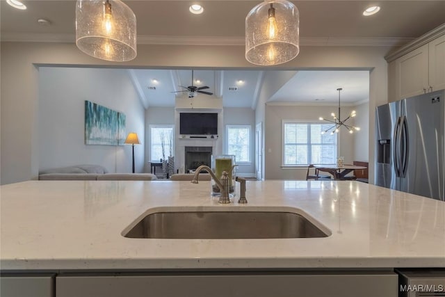 kitchen featuring stainless steel fridge, decorative light fixtures, ceiling fan with notable chandelier, light stone counters, and sink