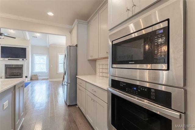 kitchen featuring white cabinets, appliances with stainless steel finishes, ceiling fan, ornamental molding, and hardwood / wood-style flooring