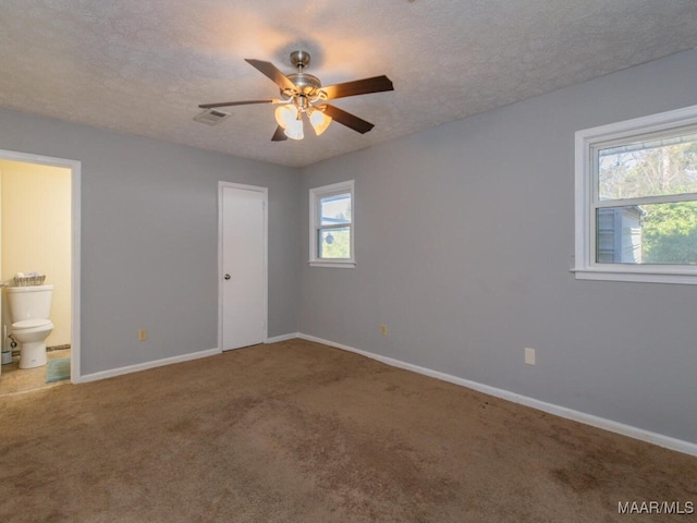 unfurnished bedroom featuring ceiling fan, multiple windows, ensuite bathroom, and carpet floors