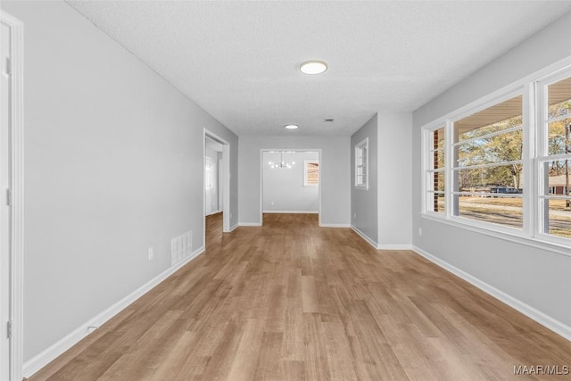 corridor featuring light wood-type flooring, a chandelier, and a textured ceiling