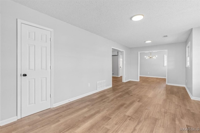 spare room featuring a chandelier, a textured ceiling, and light hardwood / wood-style floors