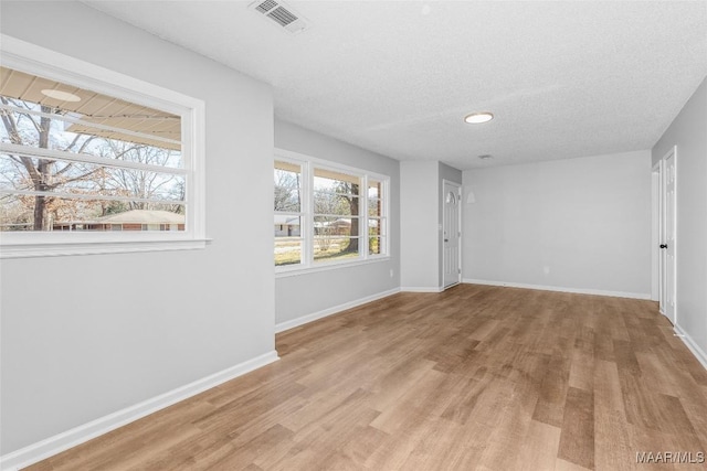 unfurnished room with light wood-type flooring, a wealth of natural light, and a textured ceiling