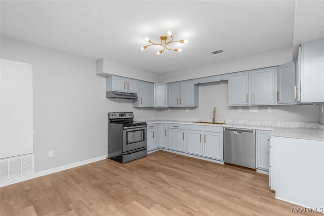 kitchen featuring stainless steel appliances, sink, gray cabinets, a notable chandelier, and light hardwood / wood-style flooring