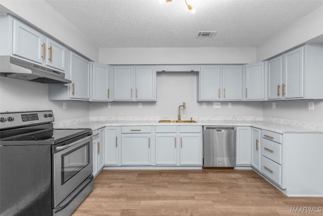 kitchen with a textured ceiling, appliances with stainless steel finishes, light wood-type flooring, and sink