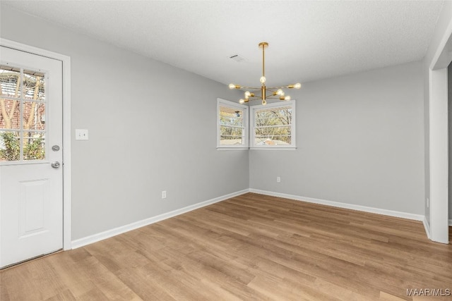 unfurnished dining area featuring a textured ceiling, a chandelier, and hardwood / wood-style floors