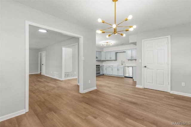 unfurnished living room featuring light wood-type flooring, sink, an inviting chandelier, and a textured ceiling