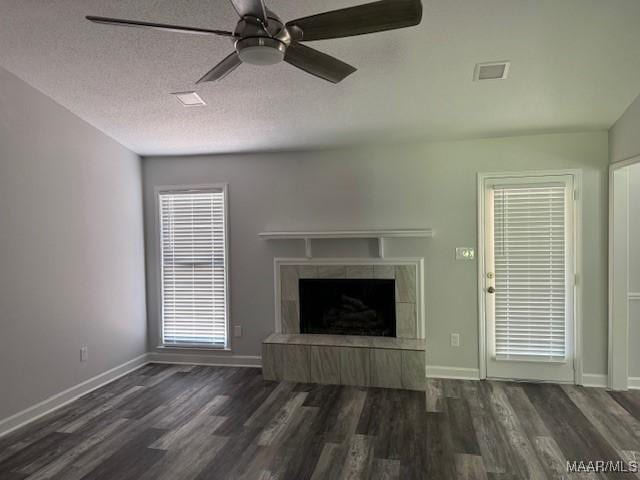 unfurnished living room featuring dark wood-type flooring, a wealth of natural light, a textured ceiling, and a tiled fireplace