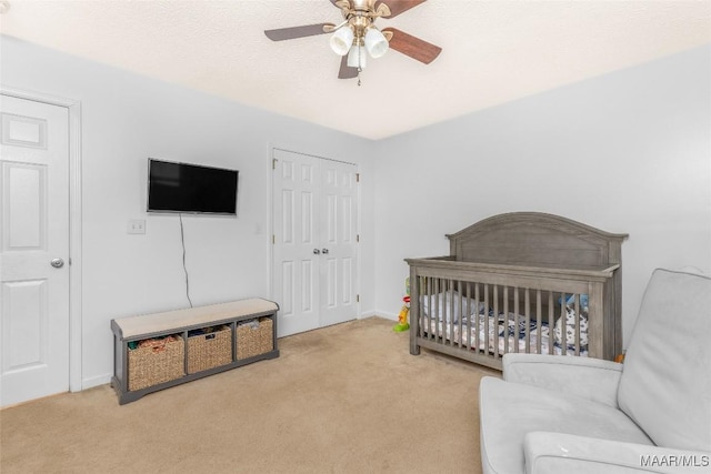 carpeted bedroom with a nursery area, ceiling fan, and a closet