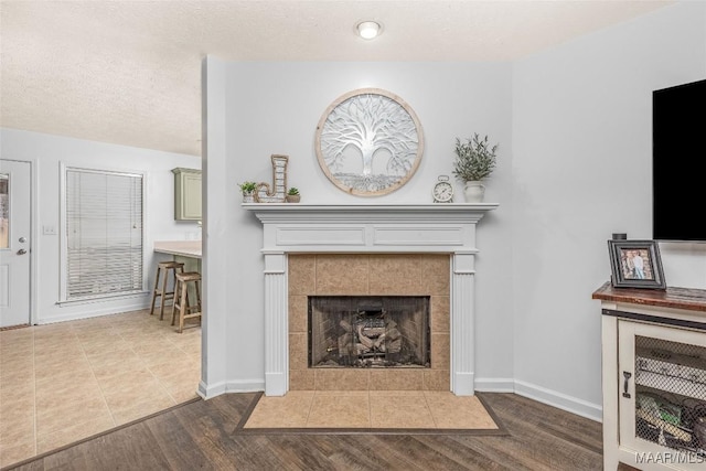 living room with wood-type flooring, a tile fireplace, and a textured ceiling