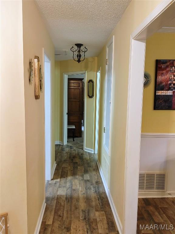 hall featuring dark hardwood / wood-style floors, a textured ceiling, and a notable chandelier